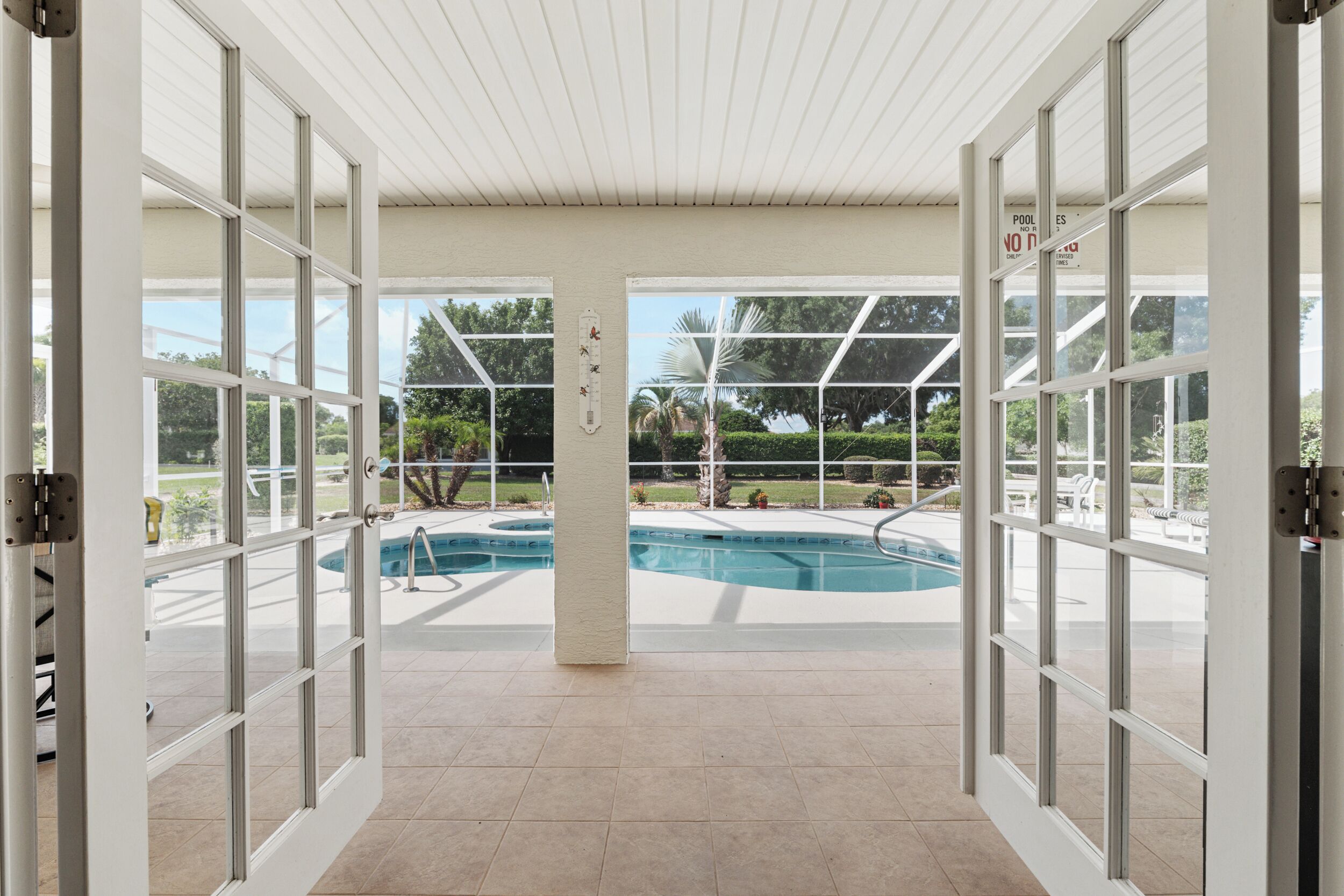 An indoor swimming pool with clear glass walls, a tiled floor, and a view of the outdoors.