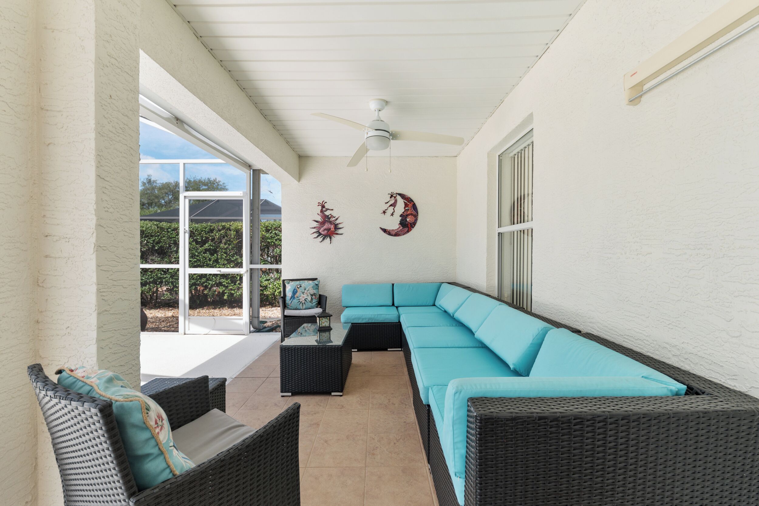 A covered patio with wicker furniture, a ceiling fan, and decorative wall art.