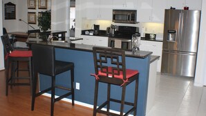 Una cucina moderna con mobili bianchi, un frigorifero in acciaio inossidabile, un forno a microonde e una macchina da caffè. Sono presenti due sgabelli da bar in legno con cuscini rossi.