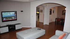 Un soggiorno con una TV a schermo piatto, un divano grigio, una panca bianca e un'area pranzo sullo sfondo.