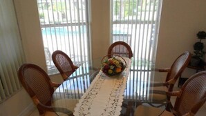 A glass-top dining table with a white lace table runner, surrounded by four wicker chairs with cushioned seats.