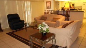 A living room with a black leather chair, a beige sofa, a white sofa, and a coffee table with a vase of flowers.