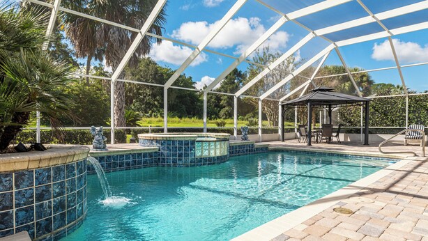 A pool area with a glass-enclosed structure, a gazebo, and a tiled edge.