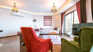 Een moderne woonkamer met een bank, twee fauteuils, een salontafel en een televisie.