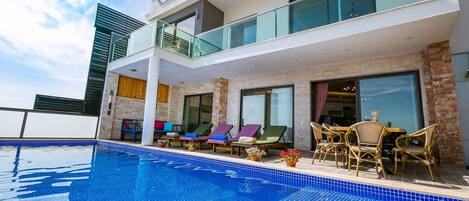 A modern hotel with a large outdoor pool, lounge chairs, and a dining area with outdoor seating.