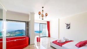 Een moderne hotelkamer met een groot bed, een rode jacuzzi, een balkon met uitzicht en een kroonluchter.