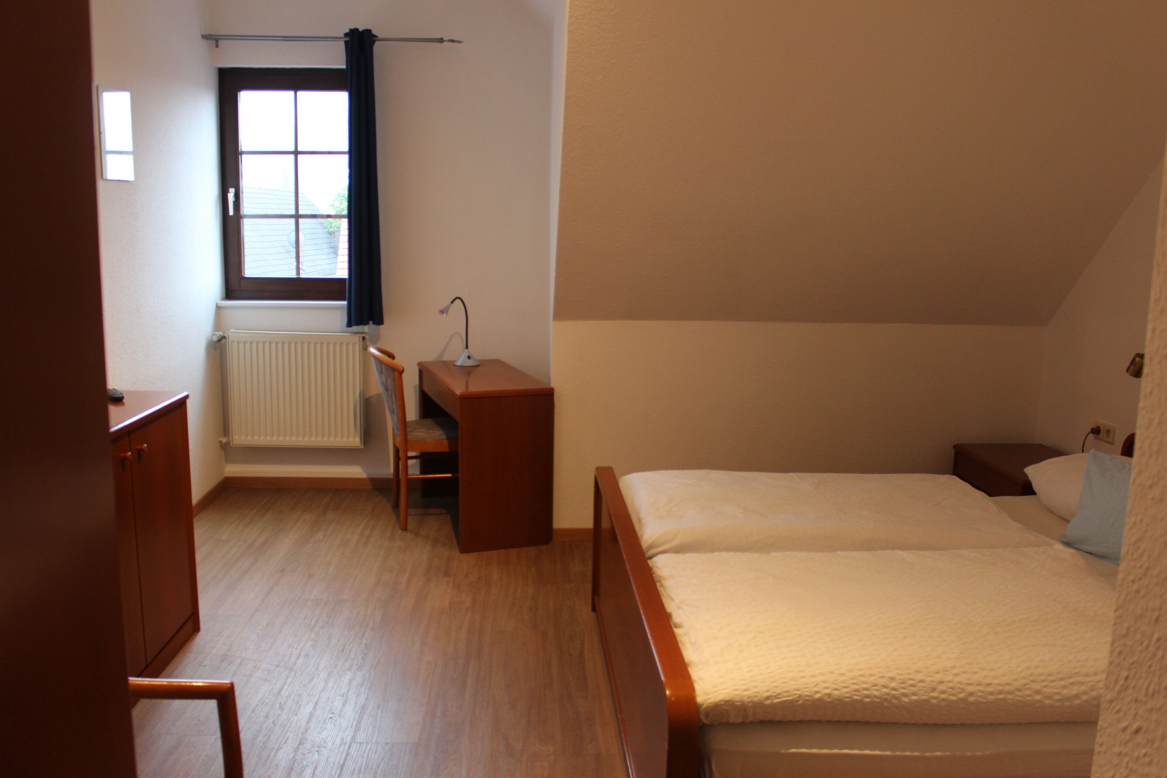 A bedroom with a bed, a desk, a chair, a radiator, and a window with curtains.