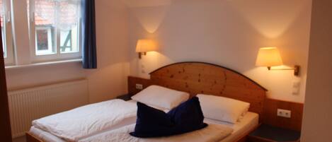 A double bed with two pillows, a nightstand with a lamp, and a window with curtains.