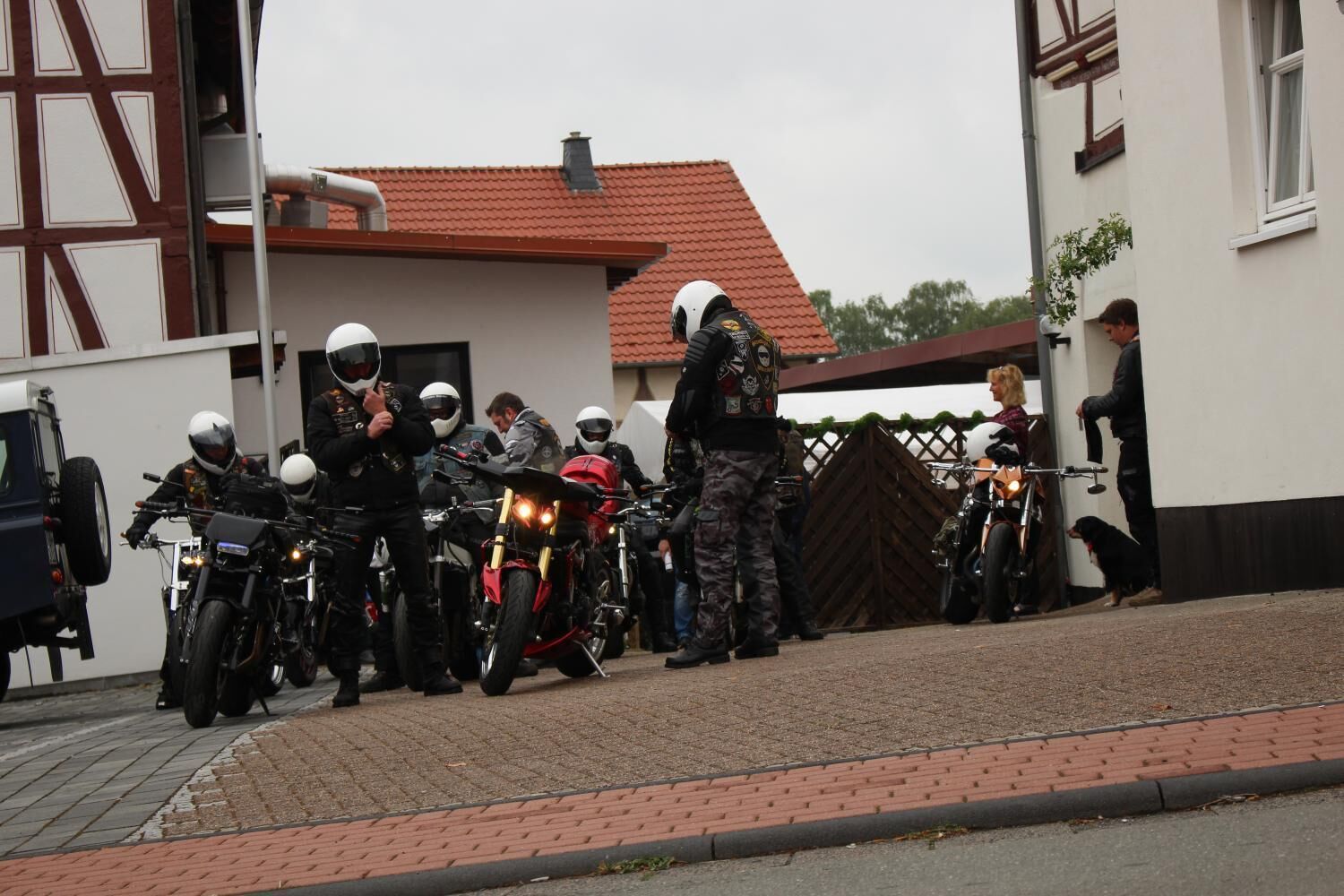 Un grupo de motociclistas reunidos frente a un edificio con techo de tejas rojas.