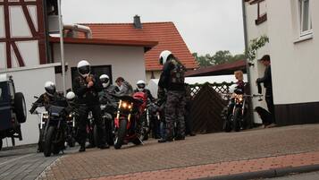 Un grupo de motociclistas reunidos frente a un edificio con techo de tejas rojas.