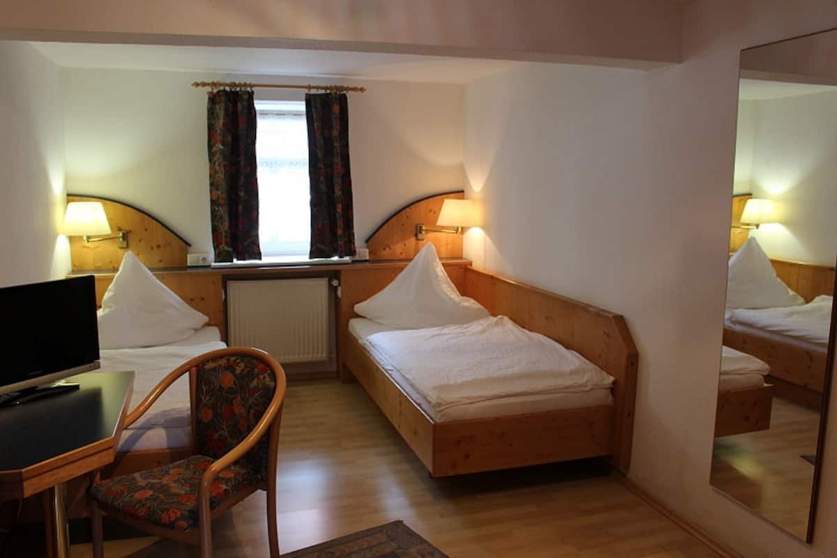 A hotel room with two single beds, a desk with a chair, a television, and a large mirror.