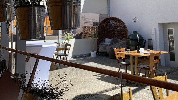An outdoor seating area with tables and chairs, potted plants, and a wicker chair. - Gasthaus Kraft (Schauenburg)