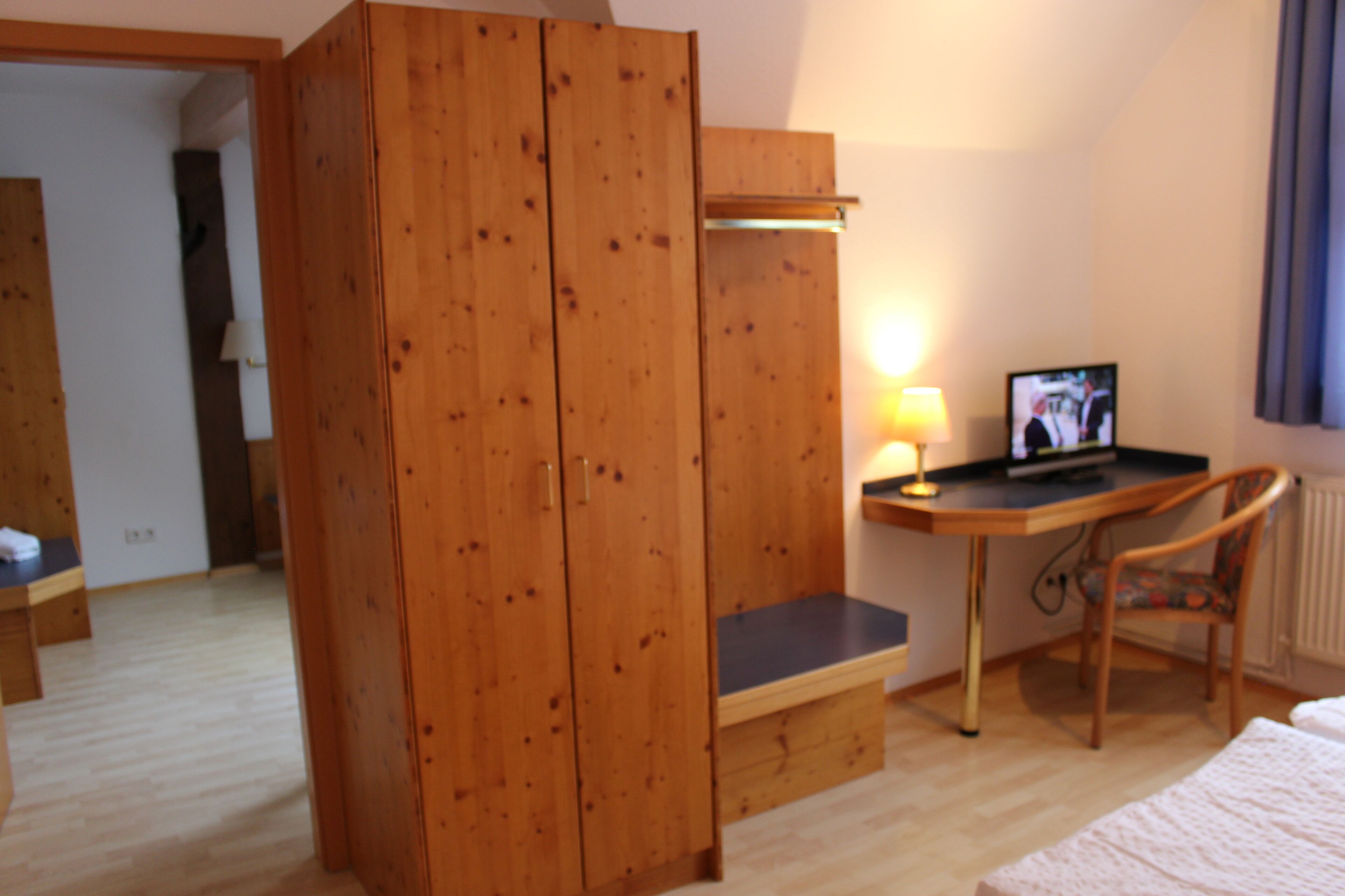 Una habitación con un armario de madera, un escritorio con una silla, una cama y un televisor.