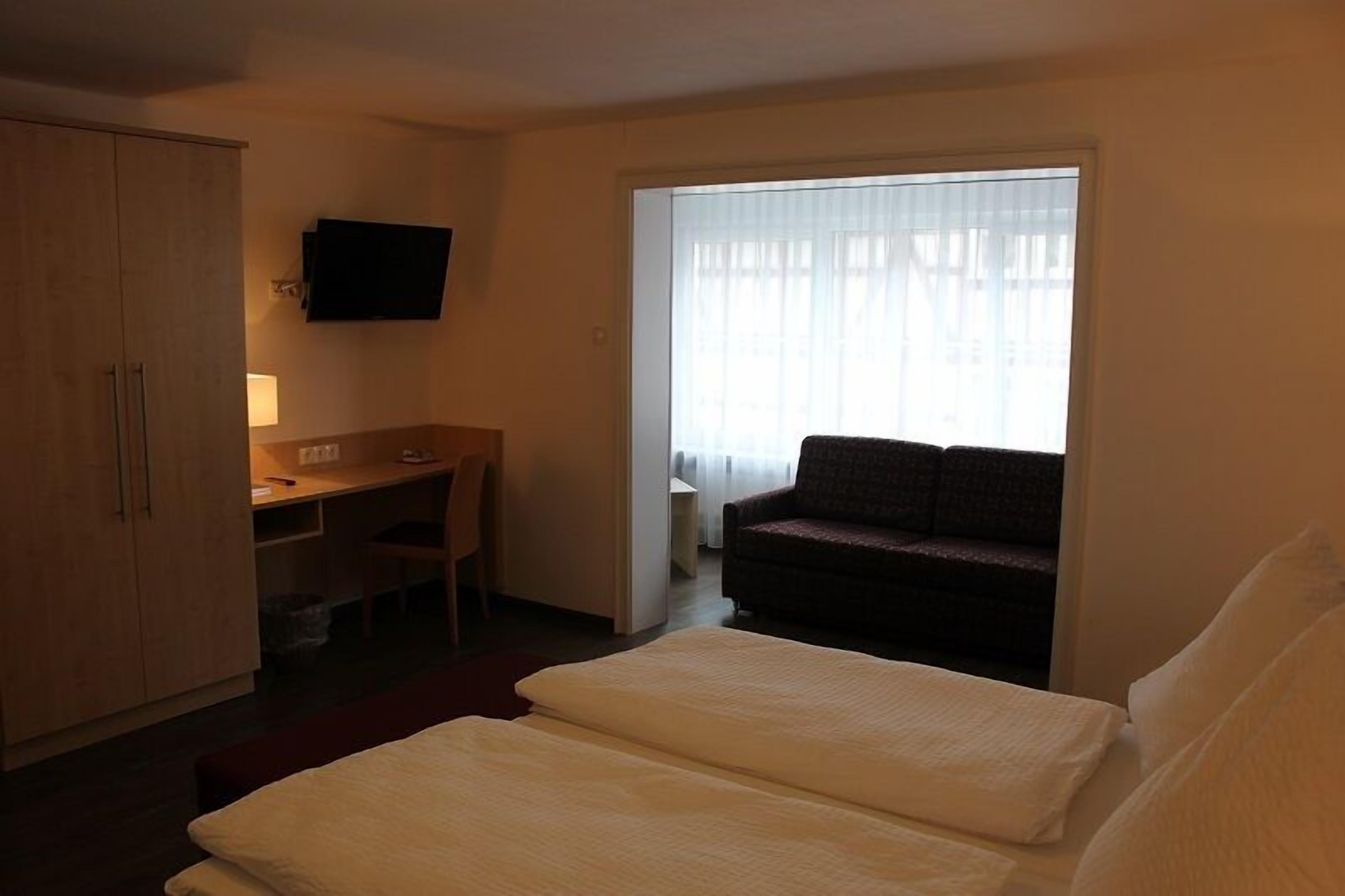 Ein Hotelzimmer mit Bett, Schreibtisch, Stuhl, Fernseher und einem fensterbepflanzten Fenster.