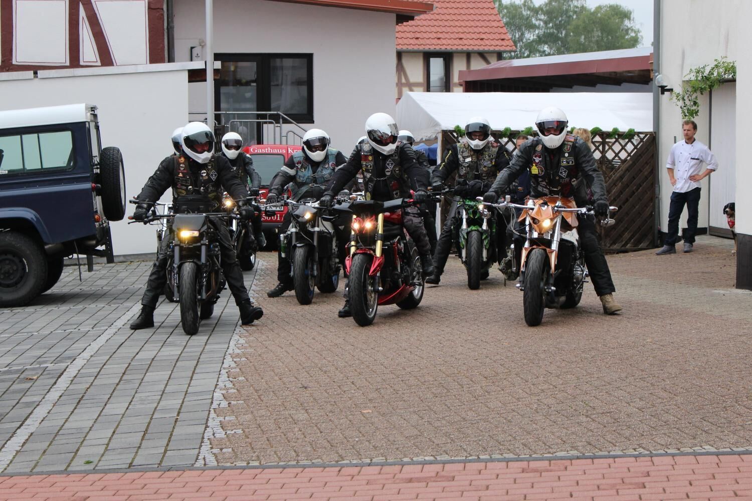 A group of motorcyclists in black gear lined up on a paved area.