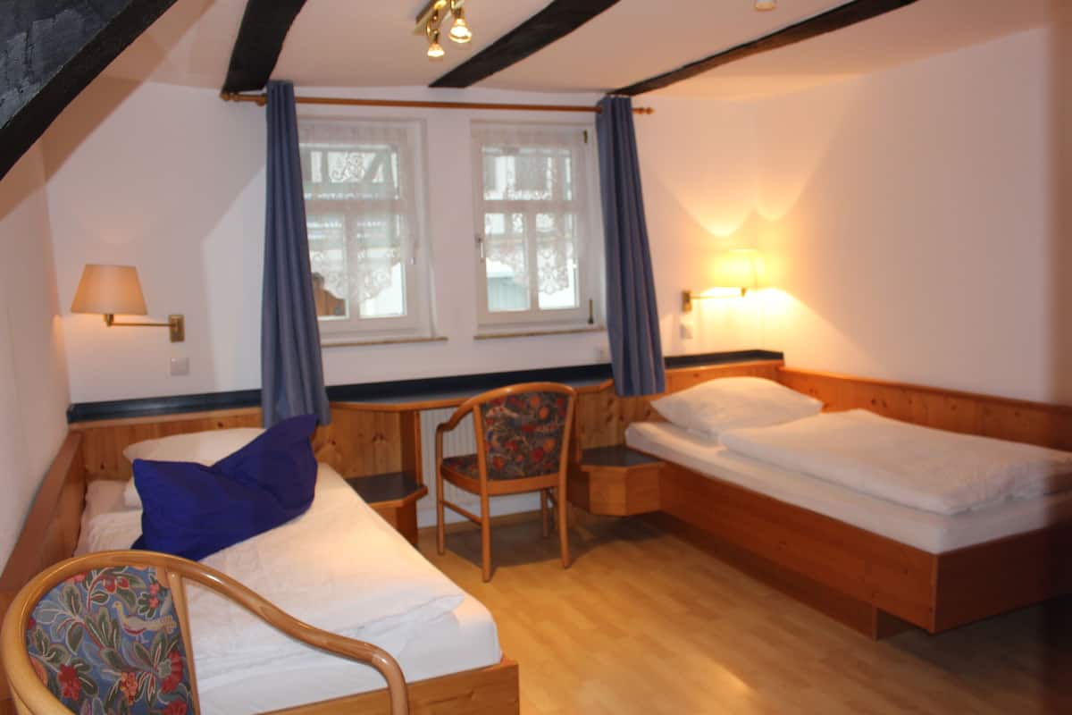 A room with two beds, a desk, a chair, and a window with curtains.