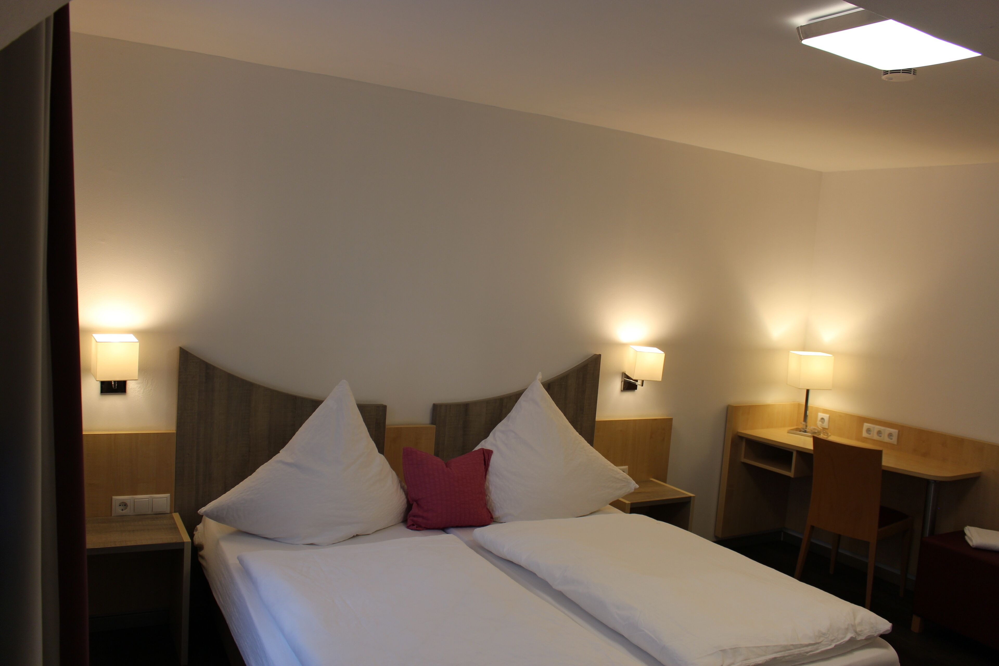 Una habitación de hotel con una cama, dos mesitas de noche, un escritorio y una silla.