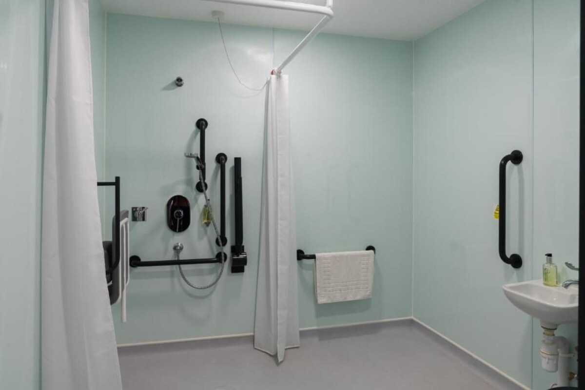 A bathroom with a shower, grab bars, a towel rack, and a sink.