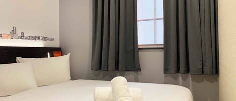 A hotel room with a bed, a window with curtains, a cityscape wall art, and a headboard.