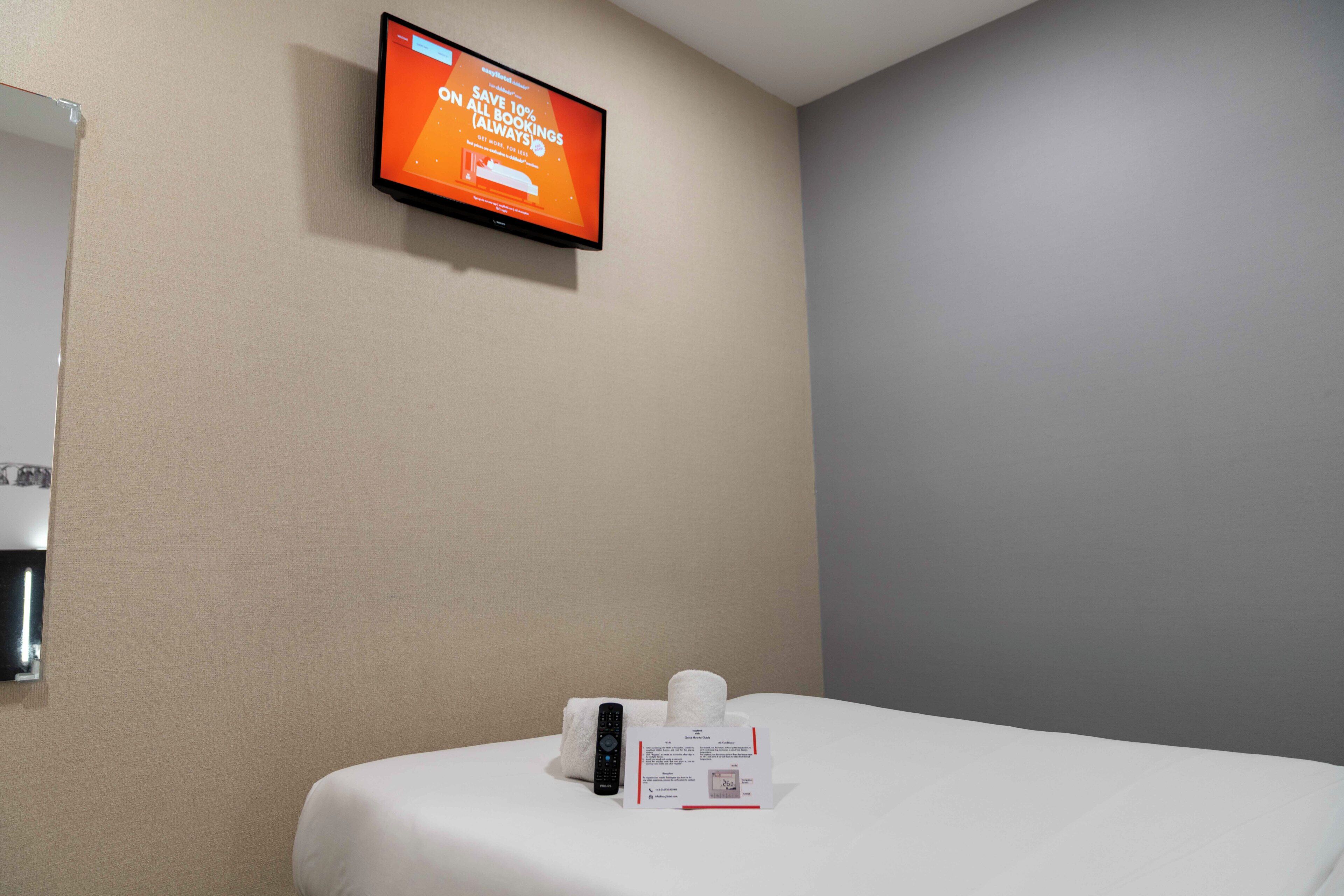 Habitació d'hotel amb un llit, un comandament a distància, una caixa de mocadors i una televisió que mostra un missatge promocional.