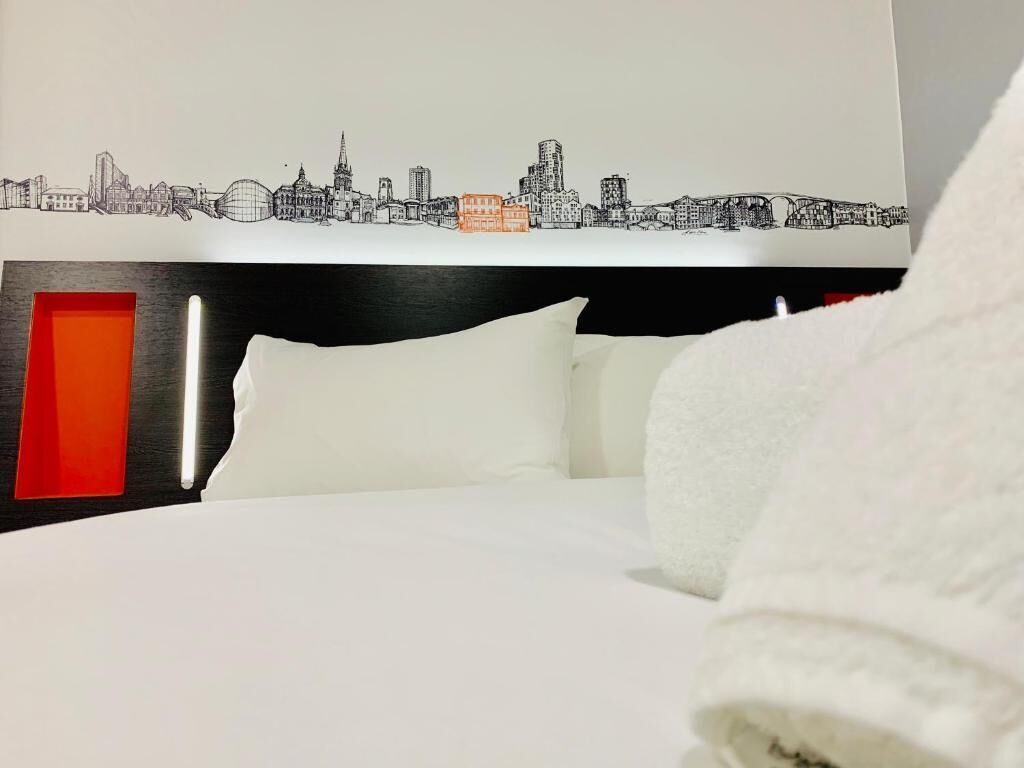 A hotel room with a bed, white bedding, a city skyline mural on the wall, and a red accent wall.