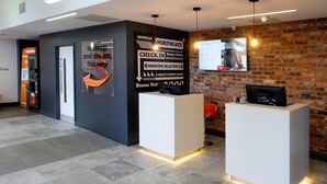 Un espace d’accueil au design moderne, comprenant un comptoir d’enregistrement, un écran numérique affichant des informations et un mur en briques.