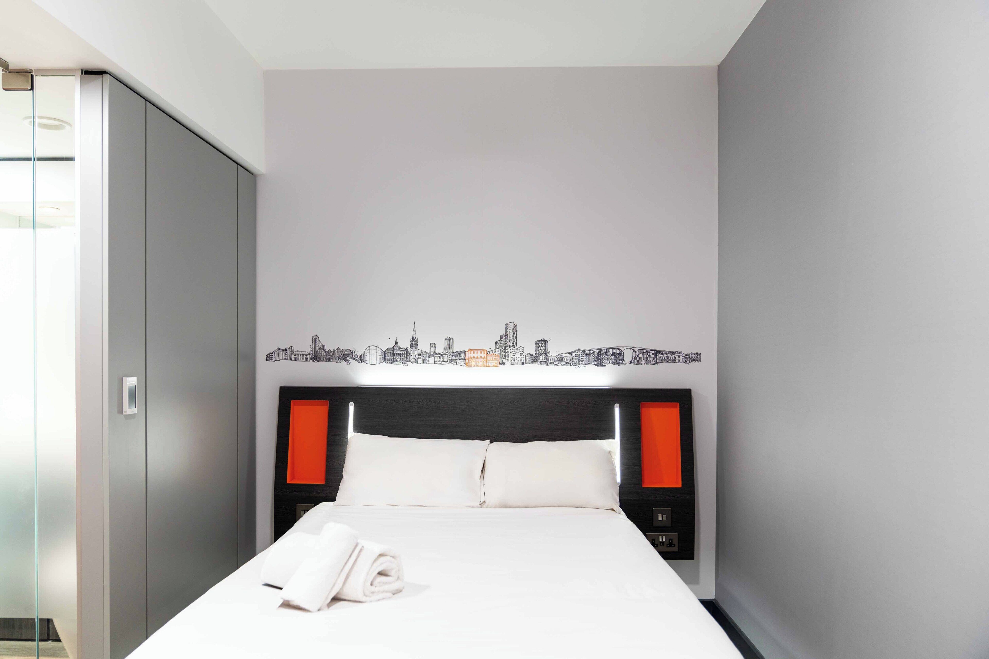 Een moderne hotelkamer met een bed, stadsgezicht kunst aan de muur, een kledingkast en een nachtkastje.
