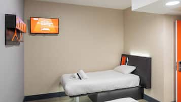 A single bed with a headboard, a television mounted on the wall, and a door to the right.