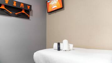 A hotel room with a bed, a TV mounted on the wall, and a towel rack with hangers.
