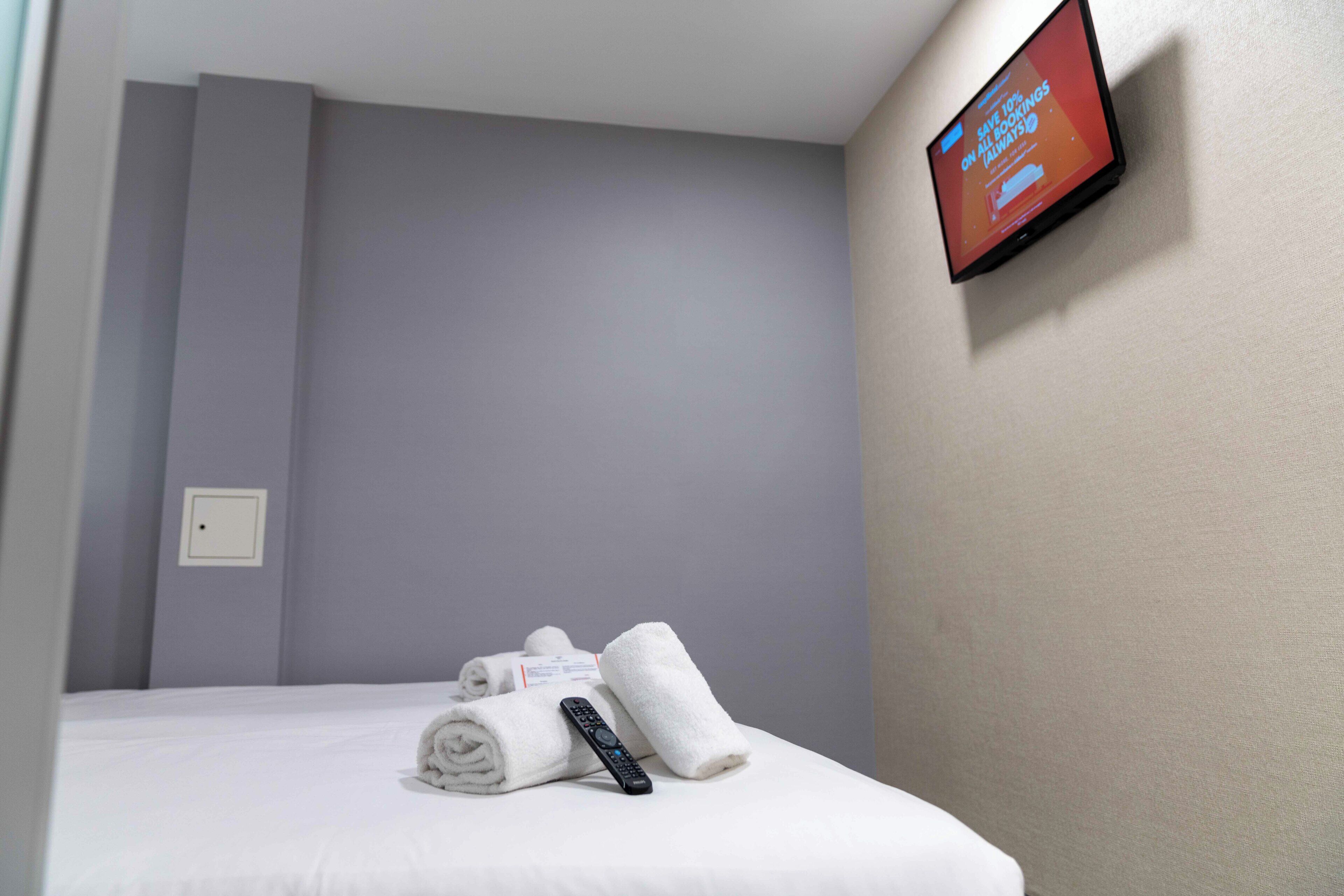Quarto de hotel com uma cama, uma televisão fixada na parede e um controle remoto sobre a cama.