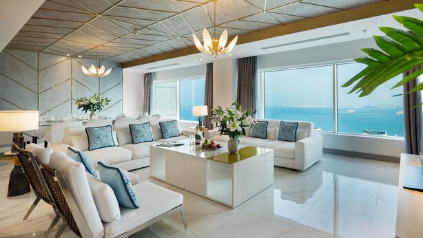 Un moderno cuarto de hotel con un ventanal que ofrece vista al mar, un conjunto de sofá blanco, una mesa de centro y una araña.
