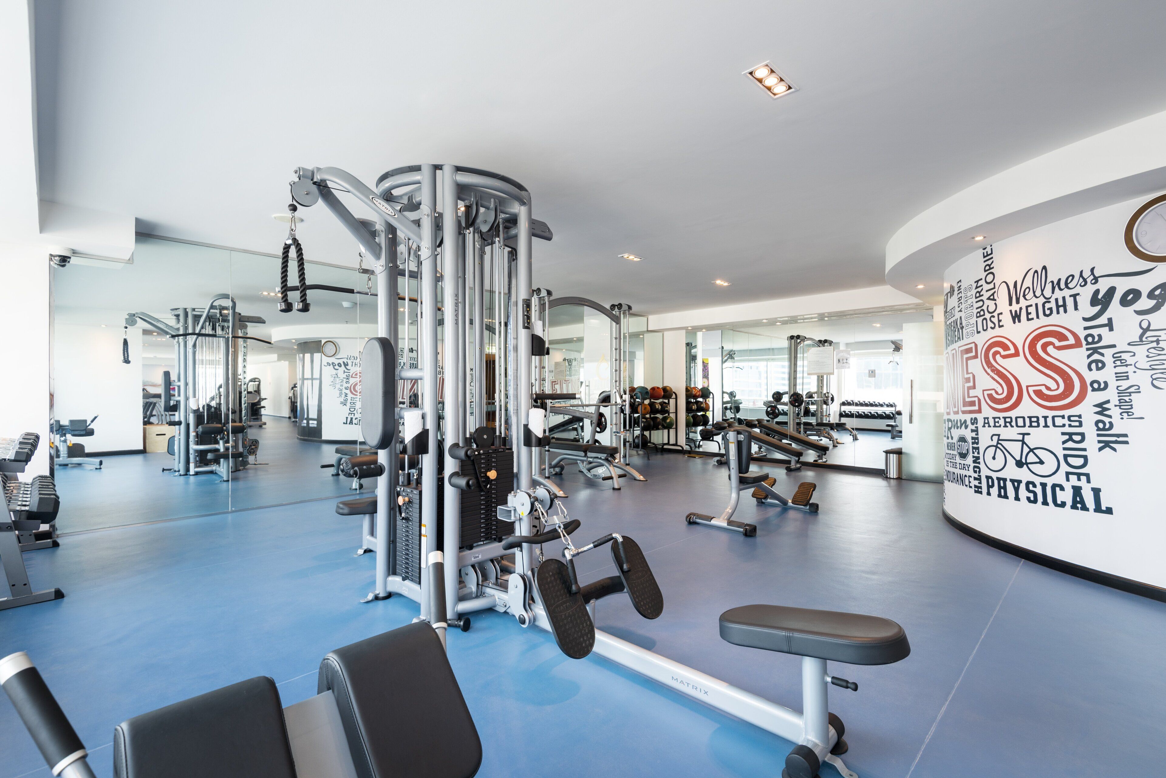 Un gimnasio con diversos equipos de ejercicio, un espejo grande y mensajes motivadores en la pared.