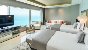 Habitación de hotel moderna con un televisor grande, dos camas, un sofá y vista al mar.