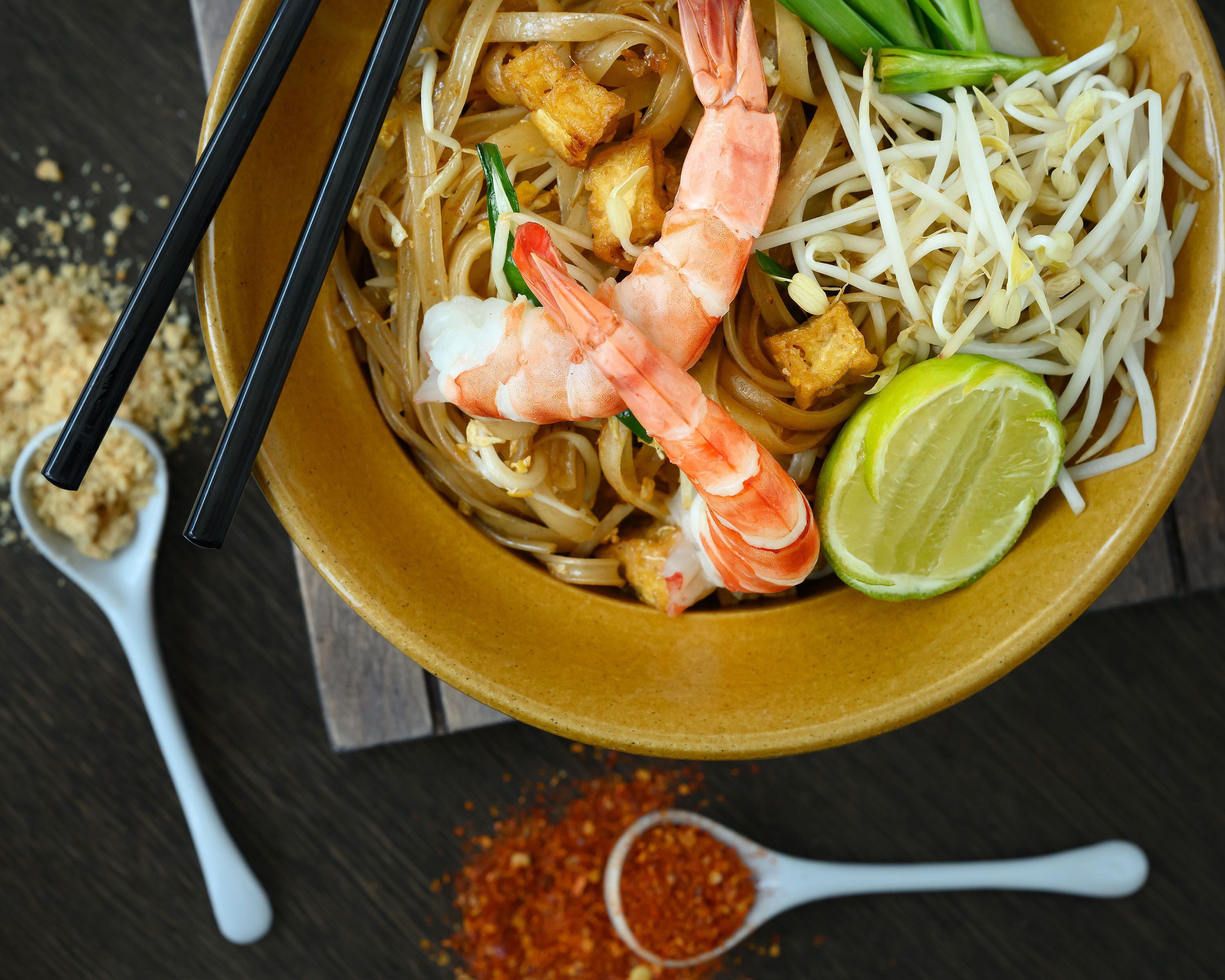 Un tazón de fideos con camarones, brotes de soja, lima y cebollas verdes.