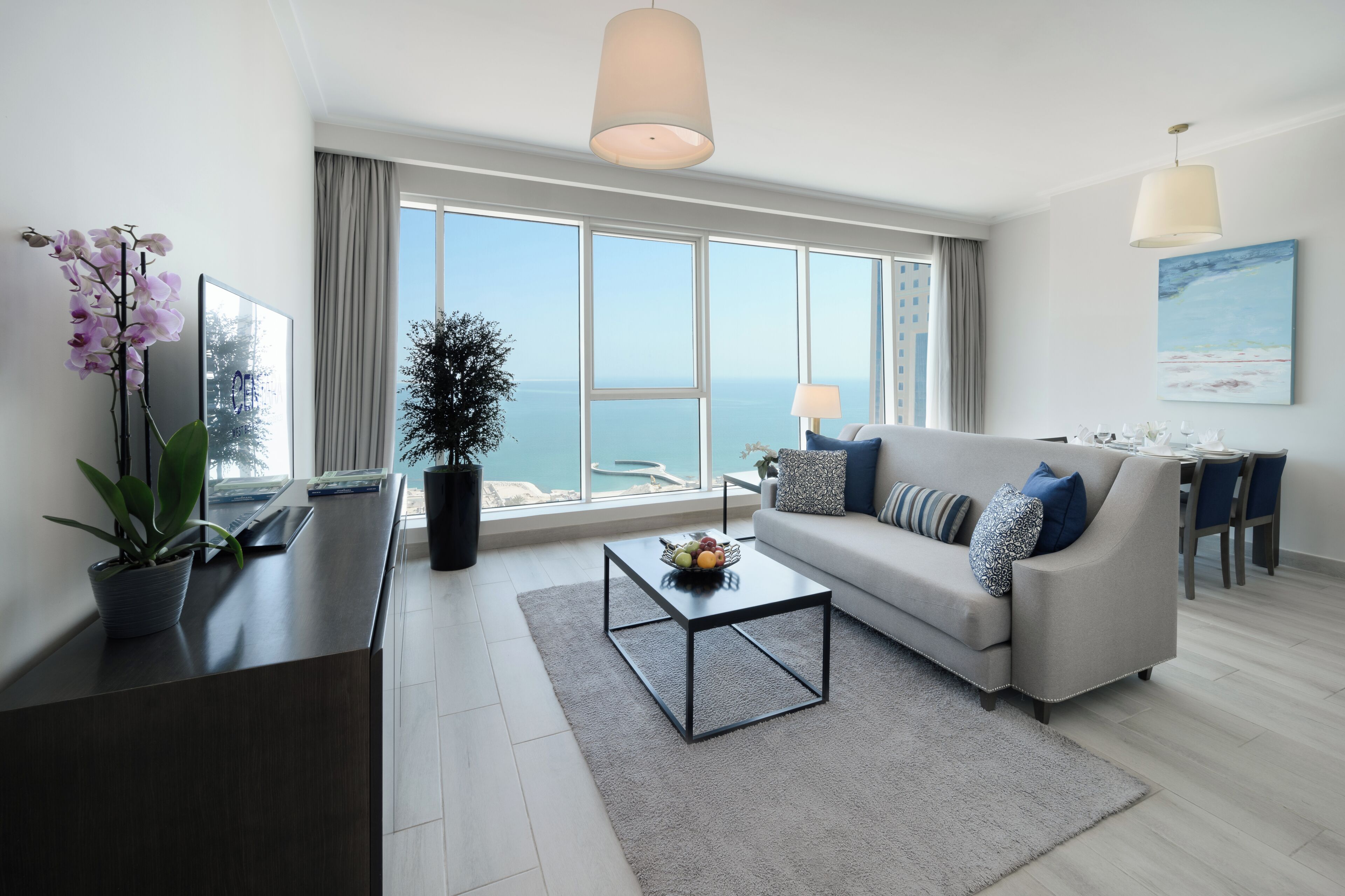 A modern living room with a sofa, coffee table, and a large window offering a view of the sea.