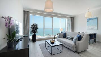 A modern living room with a sofa, coffee table, and a large window offering a view of the sea.