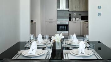 A modern dining area with a black table set for four, including plates, glasses, and cutlery. A vase with white flowers is centered on the table.
