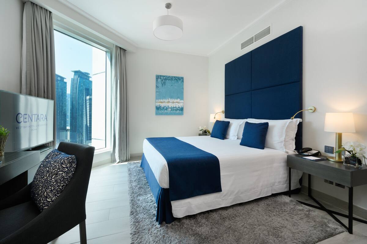 Habitación de hotel moderna con una cama grande, un escritorio con una silla, televisión y vistas a la ciudad.