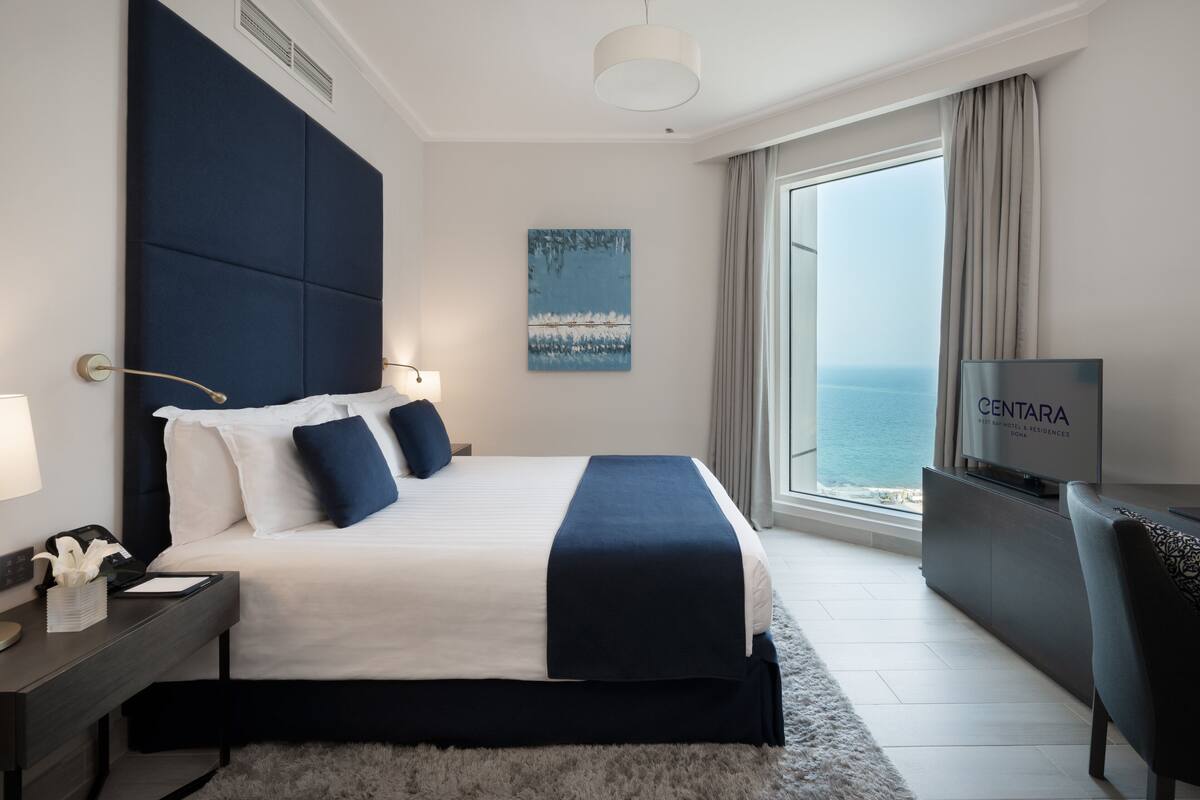 Una habitación de hotel moderna con una cama grande, un escritorio, un televisor y vista al mar.
