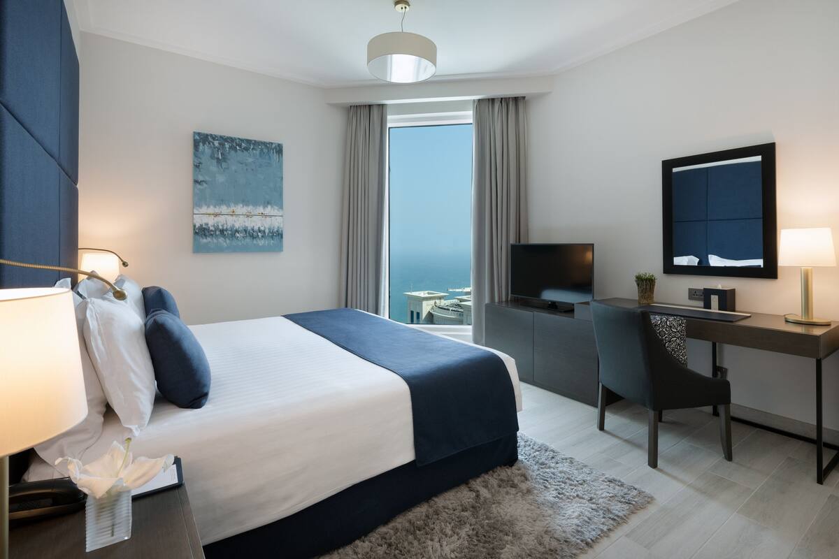 Una habitación de hotel moderna con una cama grande, un escritorio, un televisor y vistas a la ciudad.