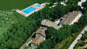 An aerial view of a property with a swimming pool, multiple buildings, and surrounding greenery.