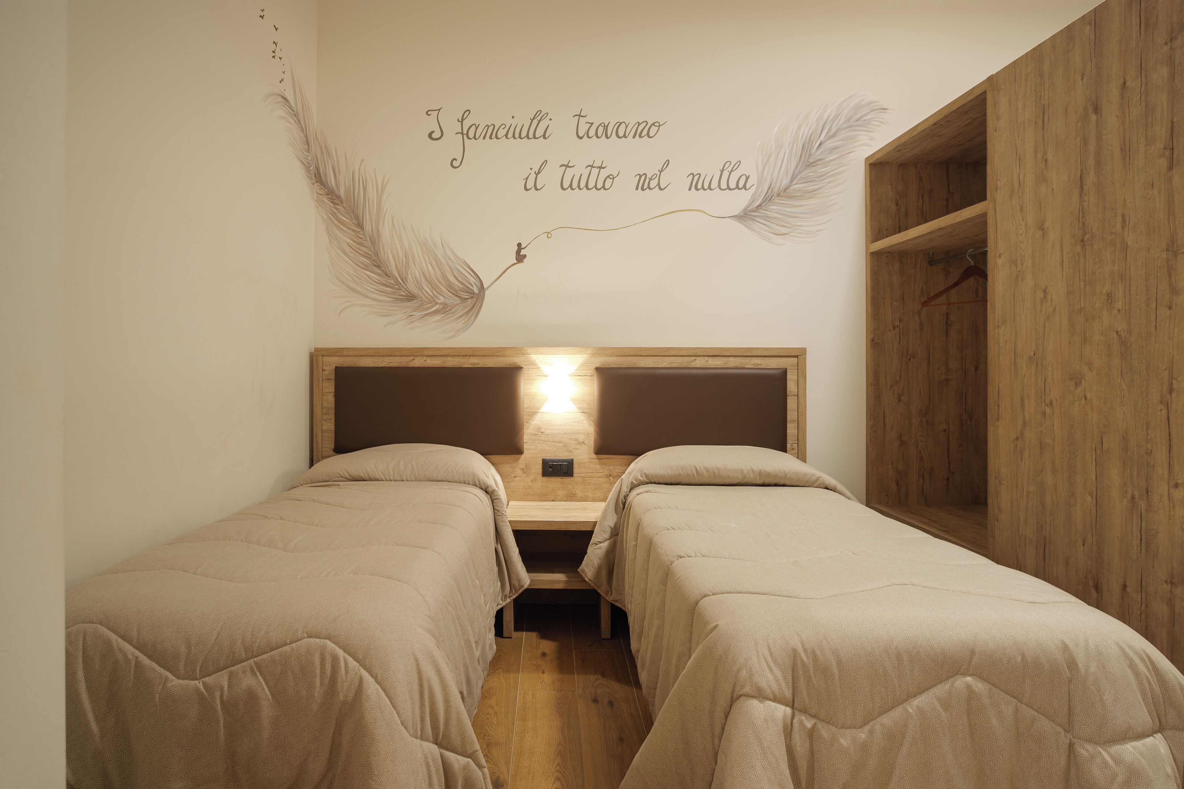 Een slaapkamer met twee bedden, een houten hoofdbord en een wanddecoratie met veertjes en tekst.