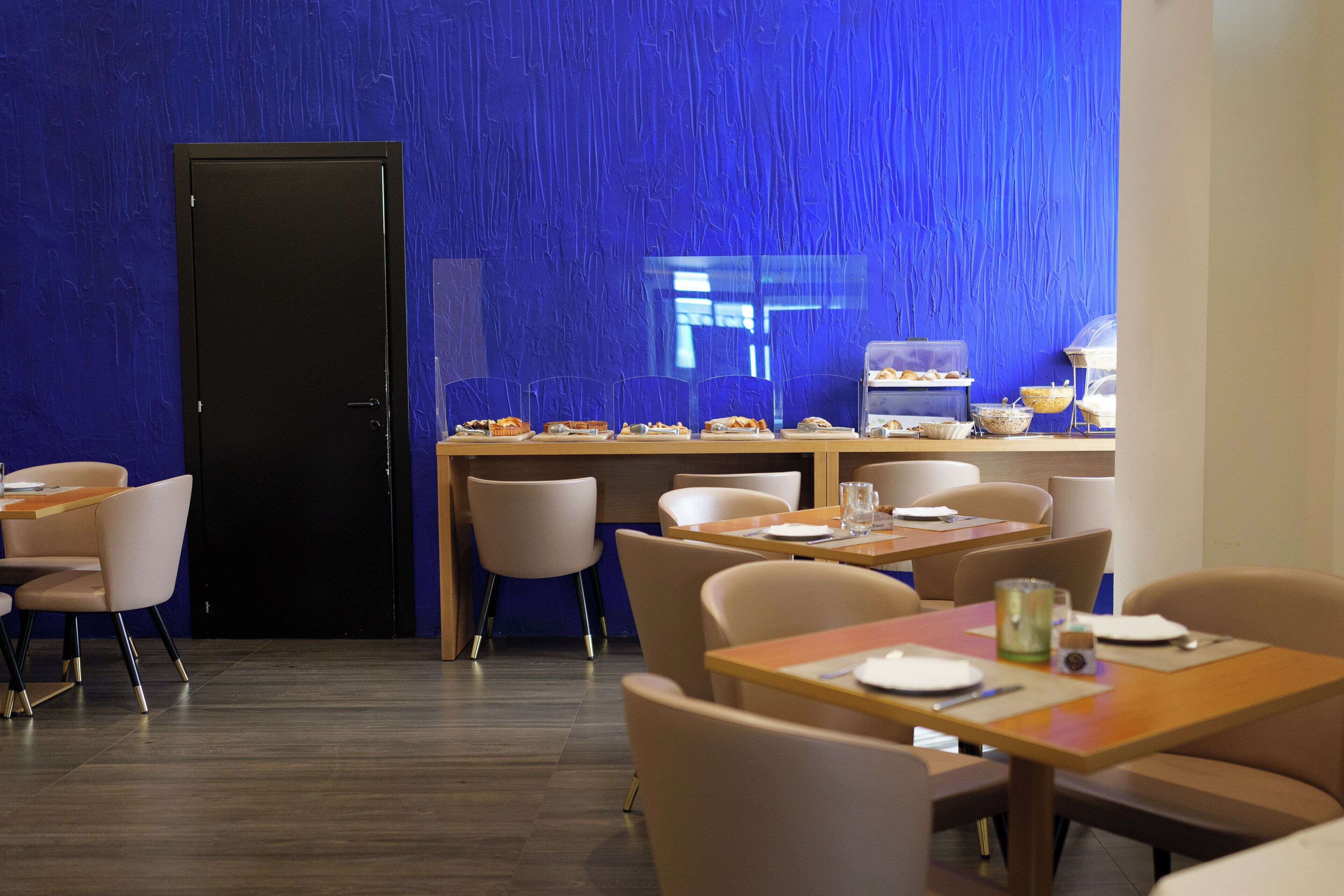 Un área de comedor moderna con pared azul con textura, mesas de madera y sillas cómodas.