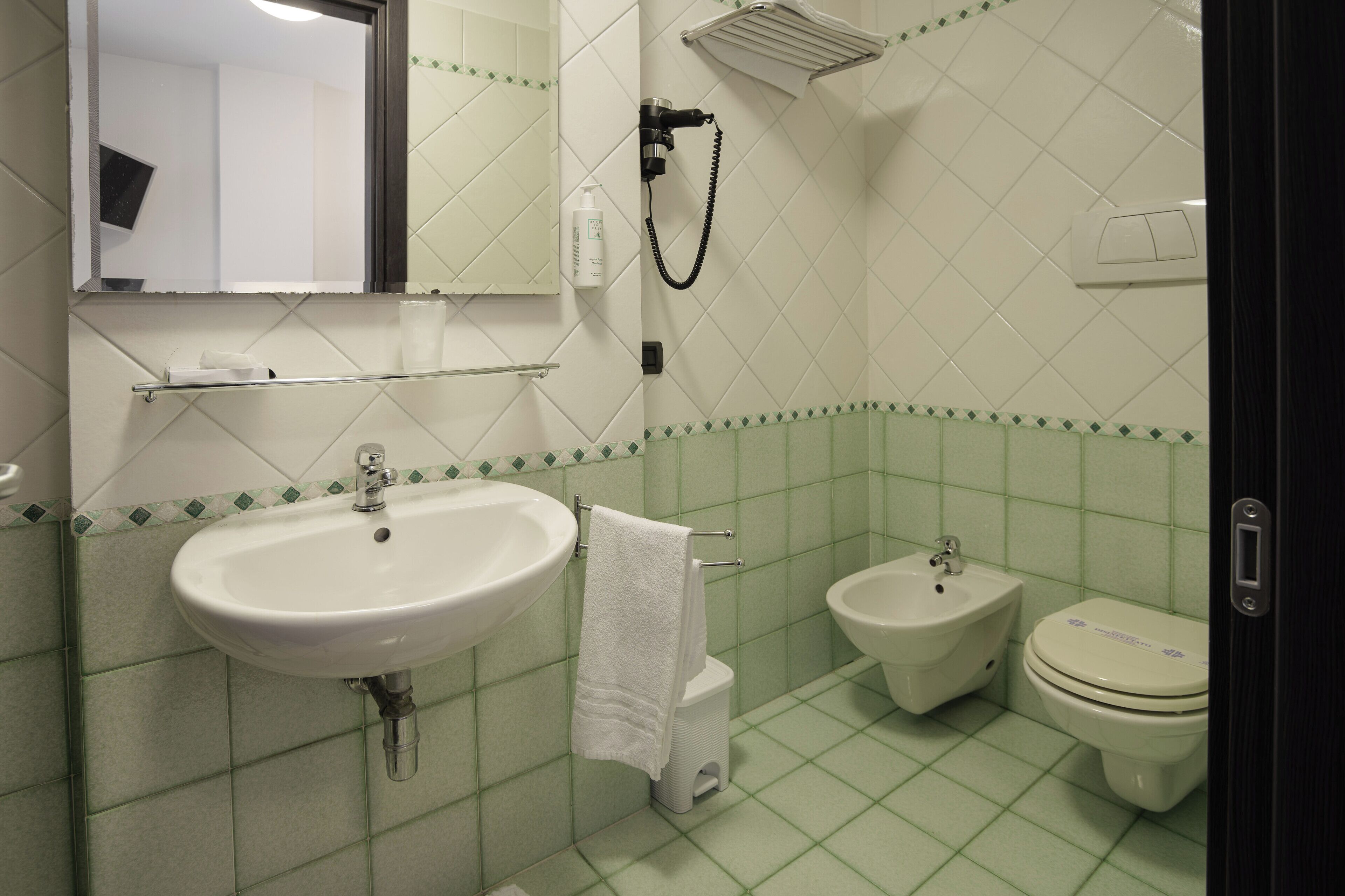 Un baño con lavamanos, bidé, inodoro y una toalla colgada en la pared.