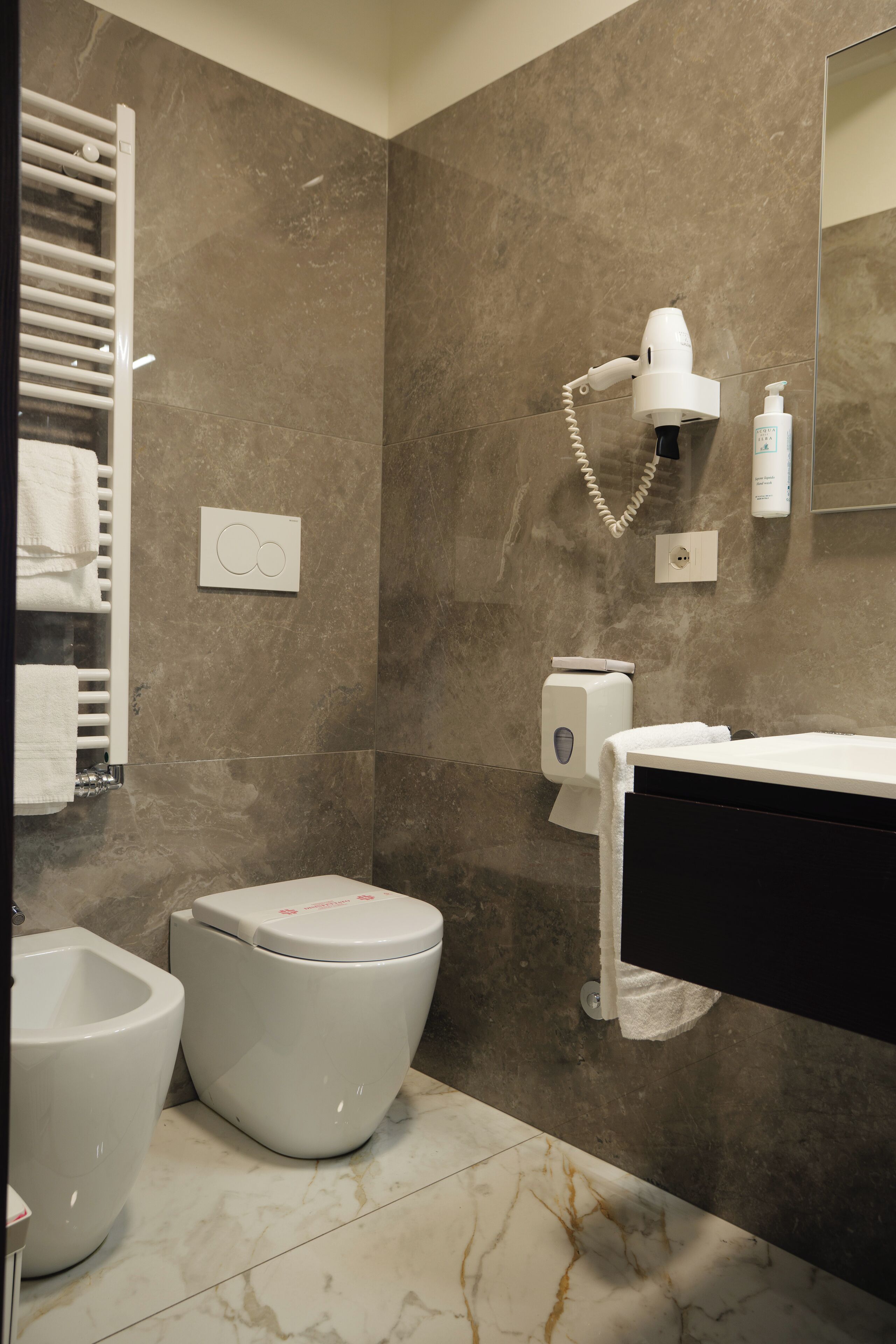 A modern bathroom with a toilet, bidet, towel rack, hairdryer, and hand dryer.