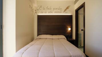 Una cama bien hecha con cabecera, una pared con una frase decorativa y un baño visible a través de una puerta.