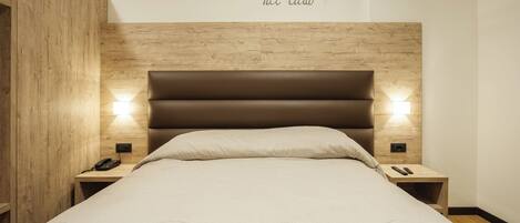 Una cama bien tendida con un cabecero, dos mesitas de noche con lámparas y una pared con una frase decorativa.