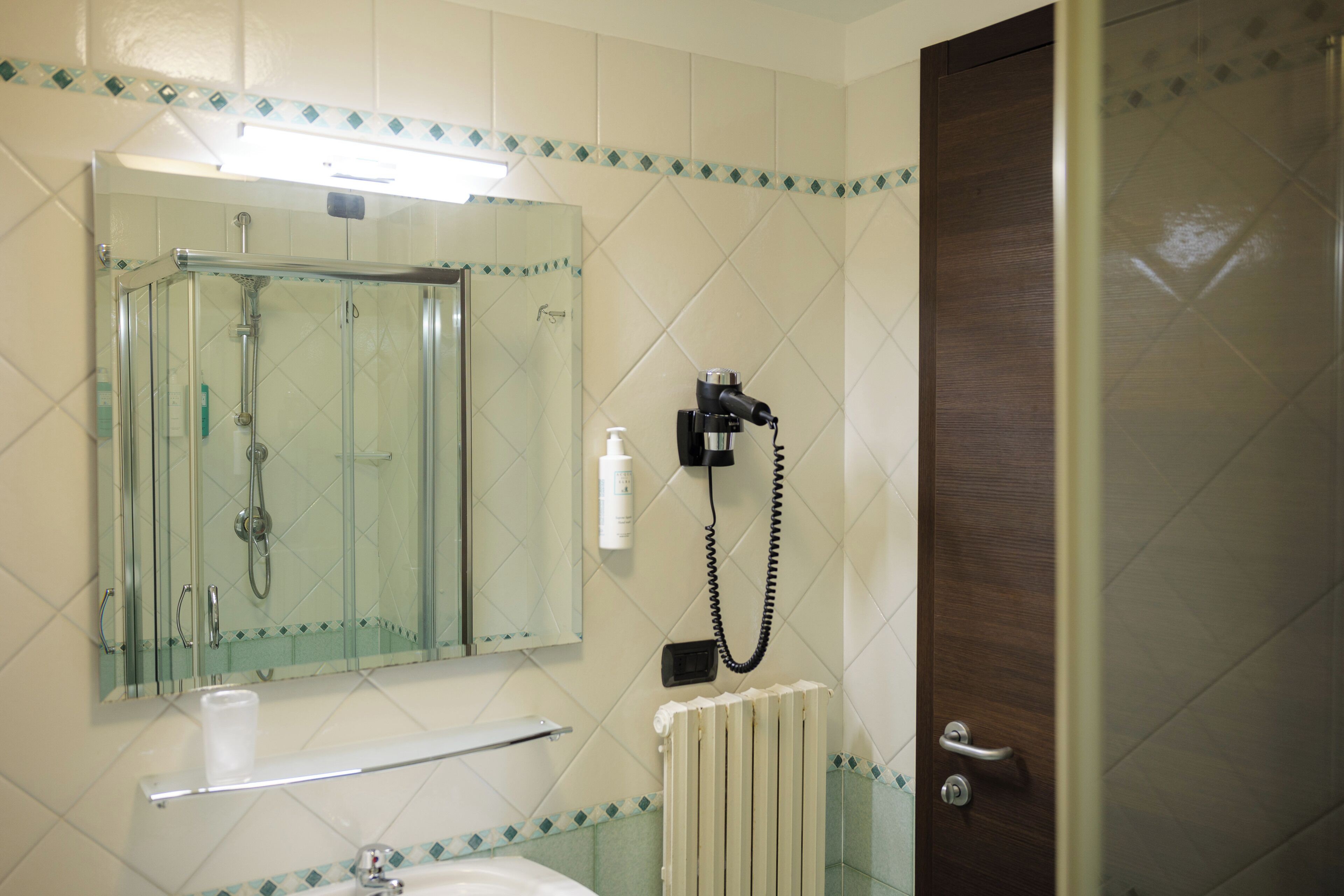 Baño con ducha envuelta en vidrio, lavamanos, espejo y toallero.