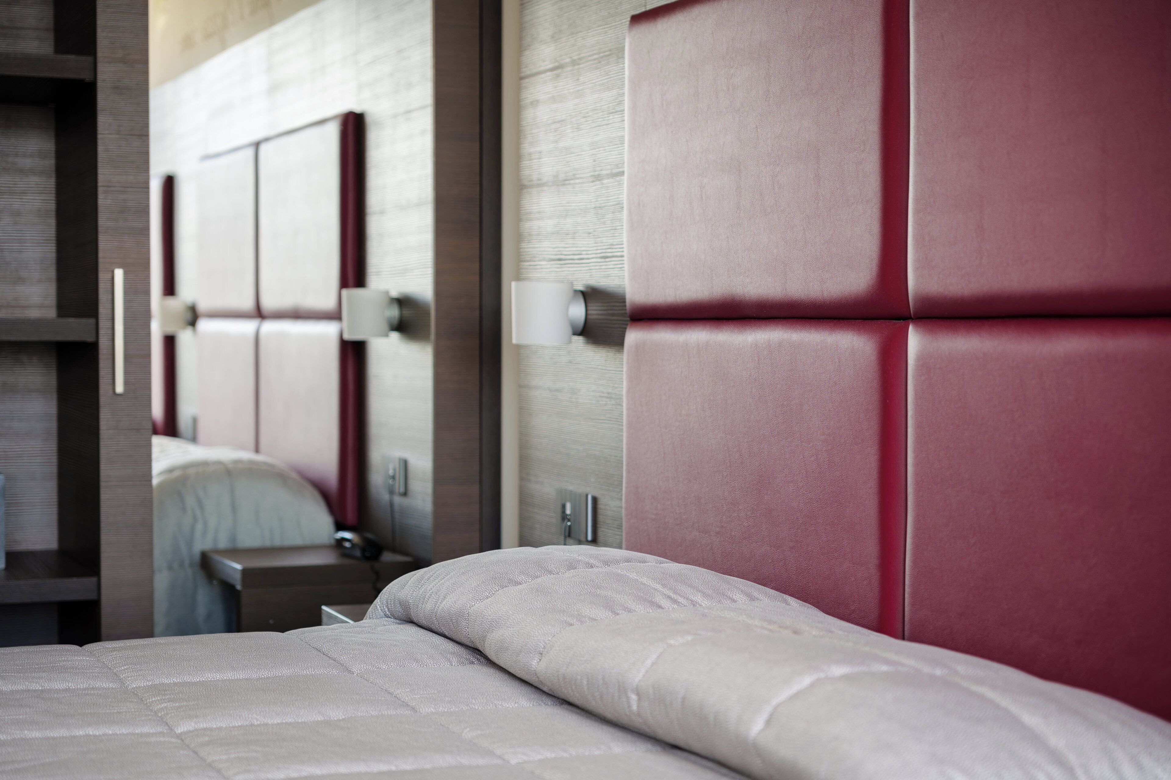 Una habitación de hotel moderna con una cama grande, una mesita de noche de madera y un cabecero tapizado en rojo.