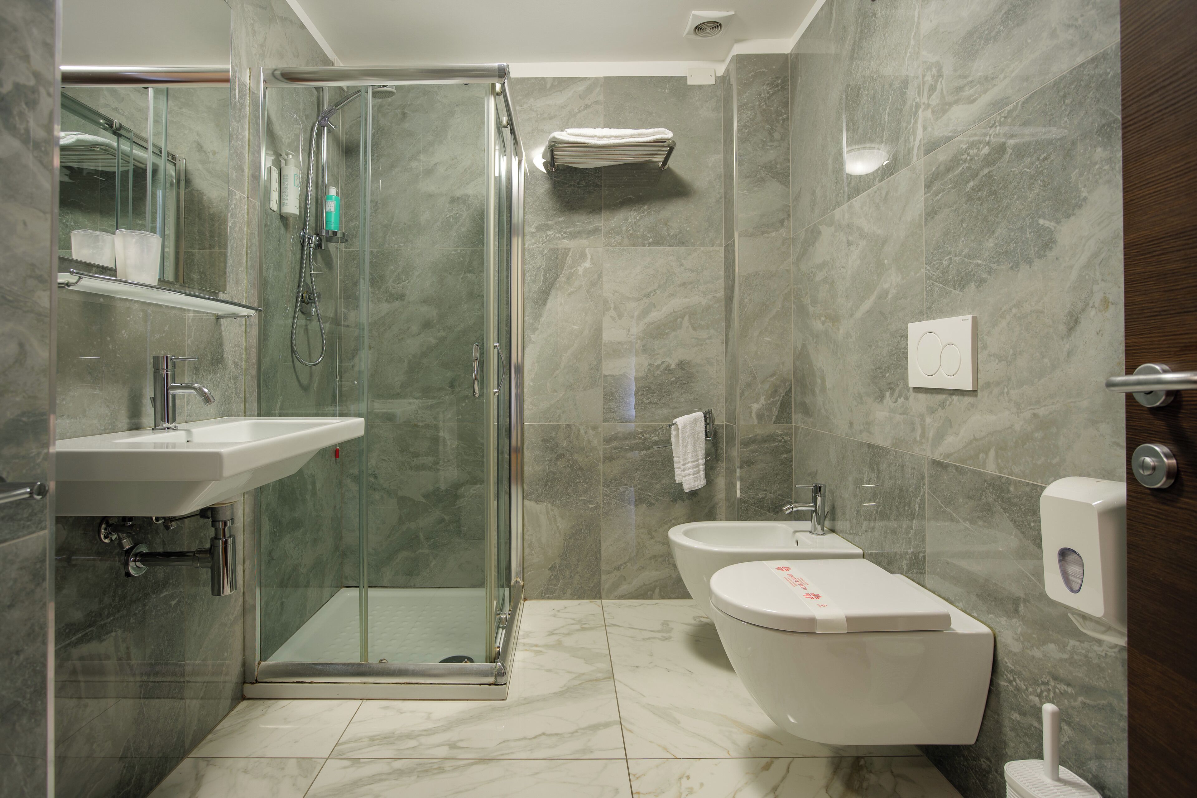 A modern bathroom with a glass-enclosed shower, a sink, a bidet, and a toilet.